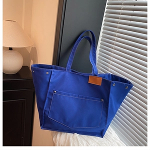 Détail du cabas en toile bleu Klein avec poche avant et finitions en rivets métalliques