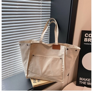 Détail du sac cabas en toile beige montrant les rivets métalliques et l'écusson en cuir