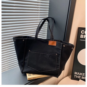 Détail du fourre-tout en toile noire avec coutures blanches et rivets sur les poches