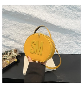 Detail of round yellow fashion handbag with embossed SM letters and top handle strap