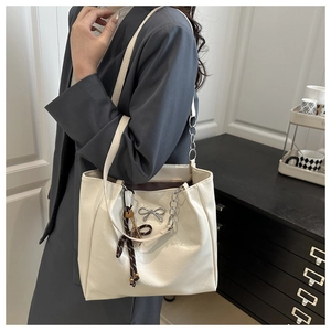 Detailed view of white tote bag with silver bow accent and tennis racket charm accessory