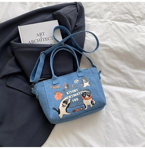 Detail of blue denim tote bag with cartoon cat illustrations and adjustable shoulder strap
