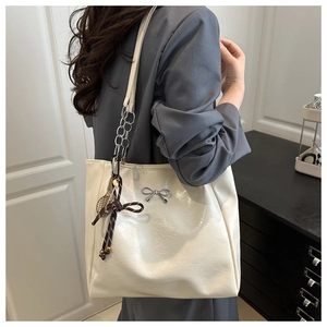 Detail of off-white glossy leather tote bag with silver bow and tennis racket charm