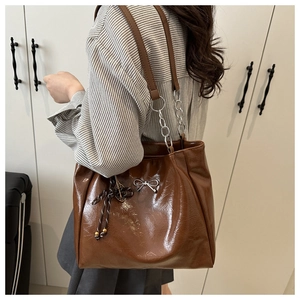 Detail of glossy brown tote bag with leather and silver chain strap on shoulder