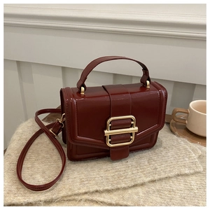 Close-up of a burgundy leather small square bag with a golden metallic buckle on a blanket