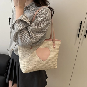 Stroh-Tragetasche mit rosa Lederherz-Patch und langem Schultergurt an einem Modell