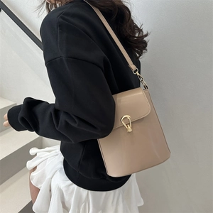Sac seau beige minimaliste avec fermoir doré porté par un mannequin en studio