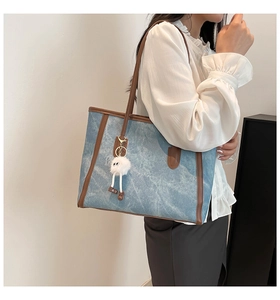 Detailed side view of large contrast tote bag with leather handles and plush monster charm