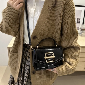 French style black glossy crossbody bag with golden buckle shown on shoulder