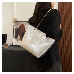 Silver crocodile pattern tote bag with gold chain strap shown on model in a cozy room