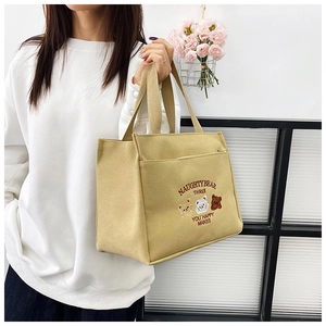 Detail of embroidered bears and text on a beige canvas tote bag with top handle