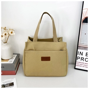 Detail of beige canvas tote bag showing brown SPORT leather patch and side zipper pocket