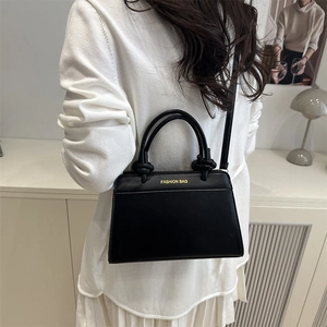Minimalist black trapezoid handbag with dual handles and gold lettering on model