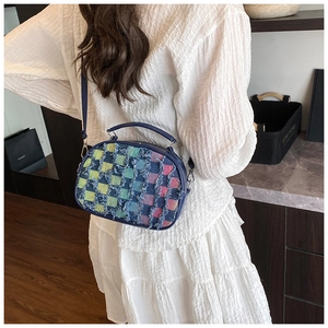 Close-up of a plaid crossbody bag with frayed fringe edges and navy blue straps