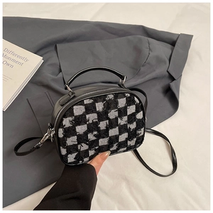 Close-up of black and white checkered tweed handbag with leather straps and metal zipper