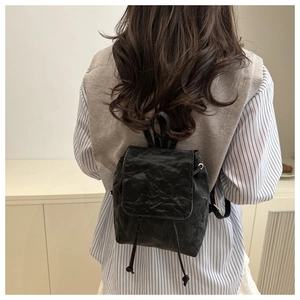Rear view of a model wearing a small black pleated backpack with drawstring flap