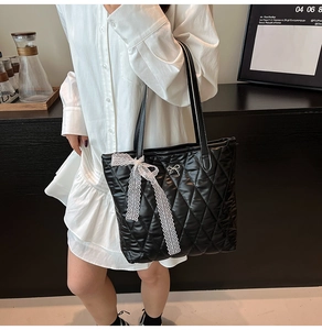 Détail du sac cabas matelassé noir avec nœud en dentelle blanche et logo doré chic