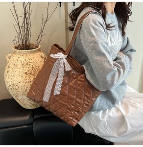 Détail d'un sac cabas marron matelassé avec nœud en dentelle blanche et logo chic