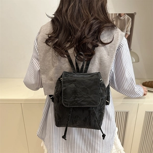 Minimalist black backpack with pleated texture and drawstring flap closure in a lifestyle setting
