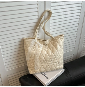 Détail du cabas matelassé beige avec nœud en dentelle et pendentif papillon en métal