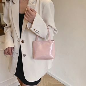 Sac fourre-tout minimaliste en cuir verni rose porté par un mannequin en costume beige