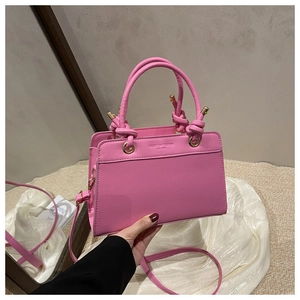 Pink faux leather tote featuring a knotted cylindrical handle and a golden metal ball closure