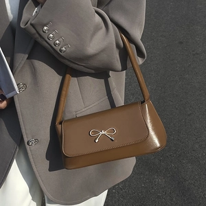 Sac baguette en cuir marron avec boucle nœud dorée porté à l'épaule par un mannequin