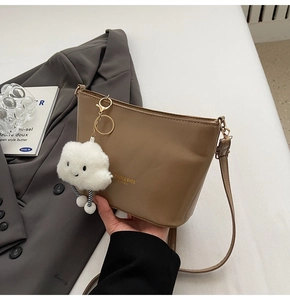 Detail of khaki bucket bag with thin shoulder strap and white cloud plush pendant