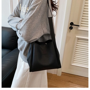 Detail of black lychee texture leather tote bag worn by a model in a minimal room