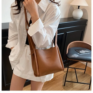 Brown litchi grain leather bucket bag featuring a Fashion embossed detail on model's shoulder