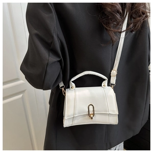 Détail d'un sac bandoulière blanc avec boucle dorée en U sur un blazer noir