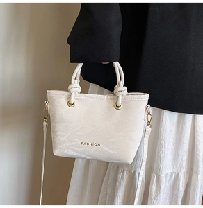 Detail of white pleated texture handbag with knot handles and gold Fashion lettering