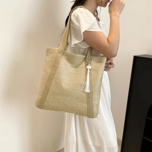 Sac fourre-tout en paille avec pompon blanc porté par une femme en robe blanche d'été