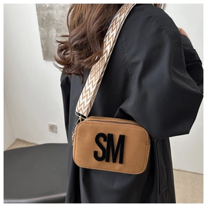 Detail of tan suede camera bag featuring 3D SM letter logo and patterned woven strap