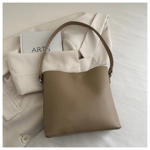 Grand sac à bandoulière kaki minimaliste posé sur un costume blanc et un livre d'art chic