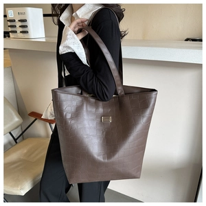 Detail of dark brown faux crocodile leather tote bag with a golden metal logo plaque