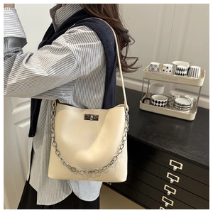 Détail du sac seau beige avec chaîne argentée et fermoir rotatif sur la bandoulière