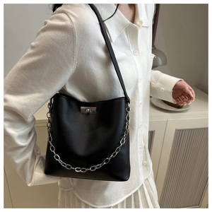 Détail du sac seau noir mat avec chaîne argentée et fermoir rotatif porté par mannequin