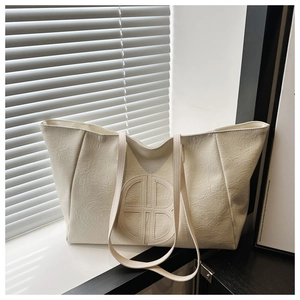 Close-up of cream white tote bag featuring a round embossed logo and lychee grain texture