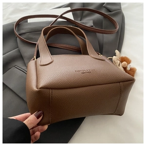 Close-up of brown litchi pattern leather bucket bag with a cute plush bear charm