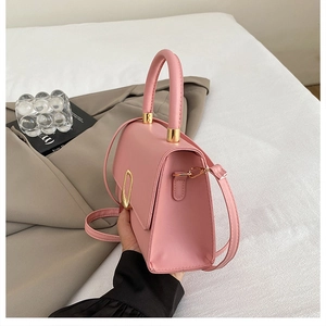 Close-up of pink leather small square bag featuring a gold ring buckle and round handle