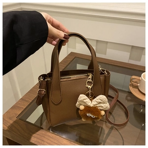 Close-up of dark brown lychee grain leather bucket bag with plush bow charm and metal zipper