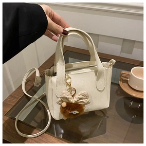 Detail of white lychee leather bucket bag with cute brown monster plush charm accessory