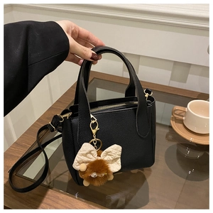 Detail of black pebbled leather bucket bag with gold hardware and plush charm pendant