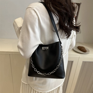 Sac seau minimaliste en cuir noir avec chaîne argentée porté à l'épaule par le mannequin