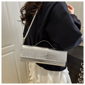 Detail einer silbernen Handtasche mit Krokodilprägung und Schultergurt für Damen
