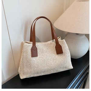 Detailed close-up of woven herringbone straw tote bag with brown faux leather handles