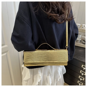 Detailansicht der goldenen Schultertasche mit Krokodilprägung am Modell in schlichter Umgebung