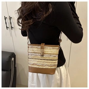 Detail of straw woven bucket bag with brown leather trim worn by a model in casual setting