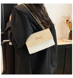 Detail of crossbody bag with beige woven flap, white leather and gold bow charm
